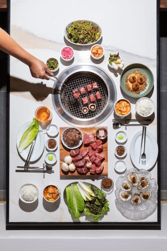 overhead view of full nuri grill feast featuring side dishes: crab fritters, oyster trio, and grilled cabbage